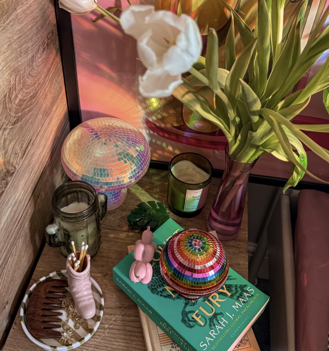 Boho shelf vignette with woven baskets, a Fury book, candles, pink vase, white tulips, and tropical plant.