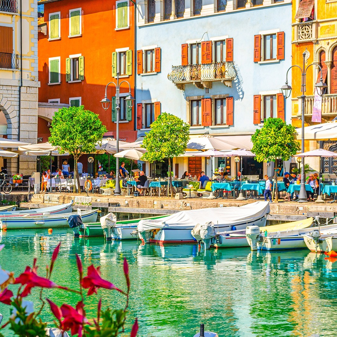 Colorful buildings and cafes along a Mediterranean harbor with boats and clear turquoise water
