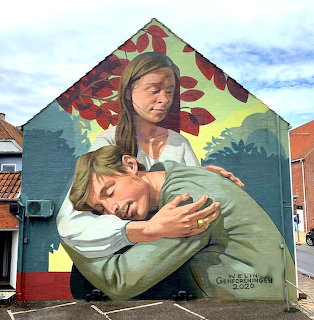Mural on a building wall depicting two people hugging with red leaves and a blue sky above