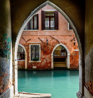 Arched view of orange brick Venetian building with turquoise canal water and weathered columns