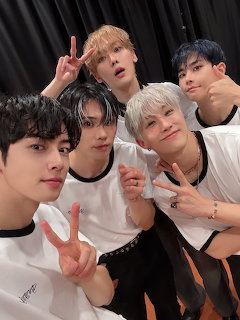 Five young men posing together for a group selfie making peace signs in white and black outfits