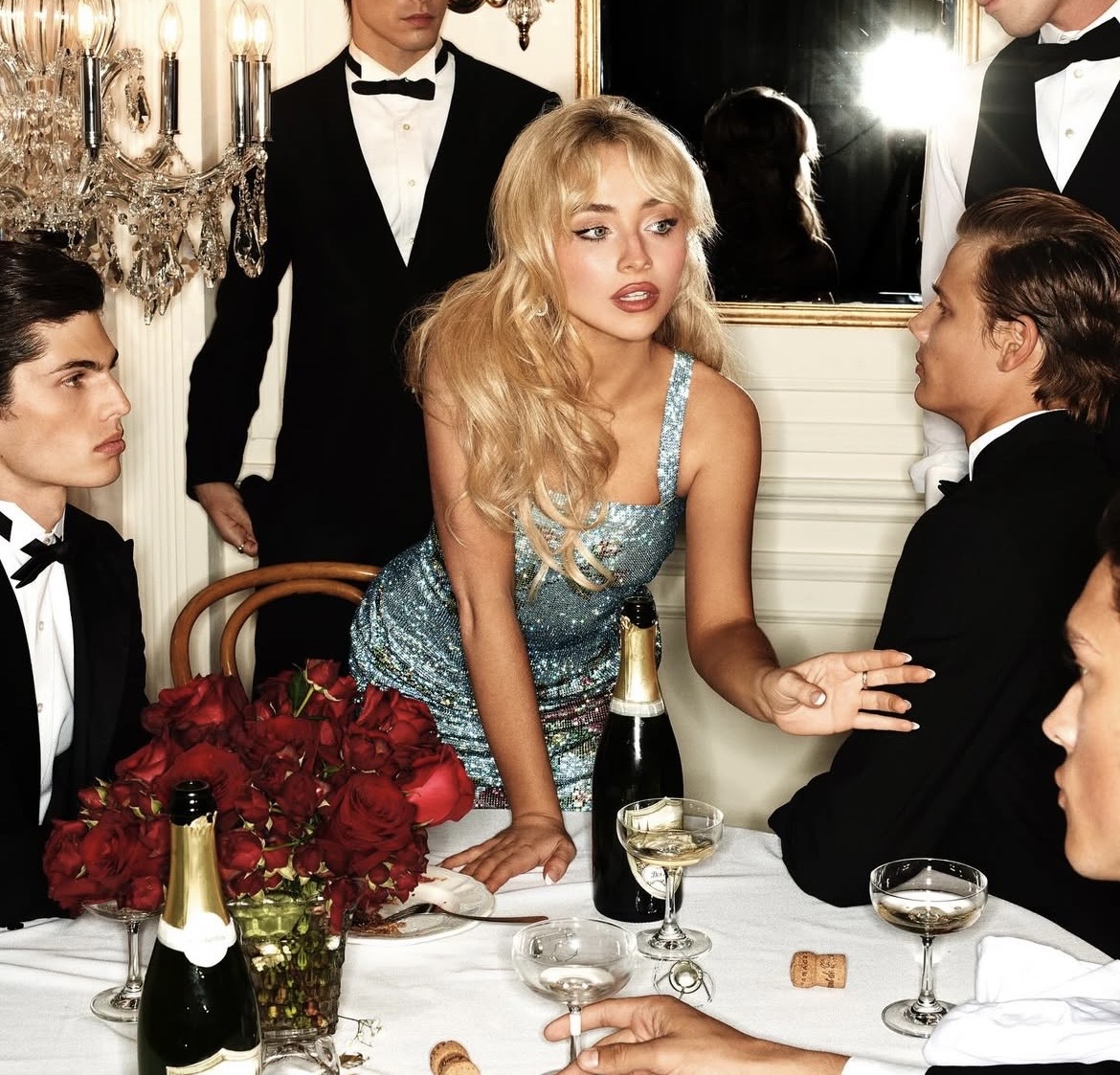 Woman in blue sequined dress at formal dinner table with tuxedo-clad guests