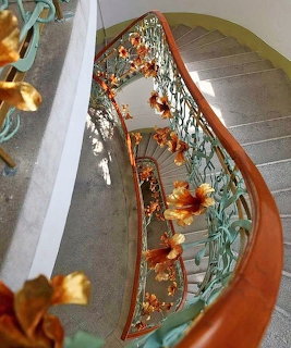 Elegant curved staircase with intricate Art Nouveau metalwork railing and golden floral details viewed from above