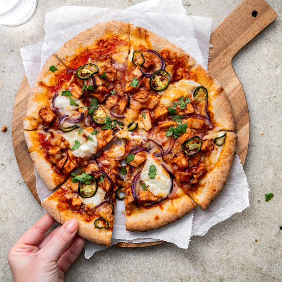BBQ chicken pizza with mushrooms, red onion, and cilantro on parchment paper over wooden cutting board