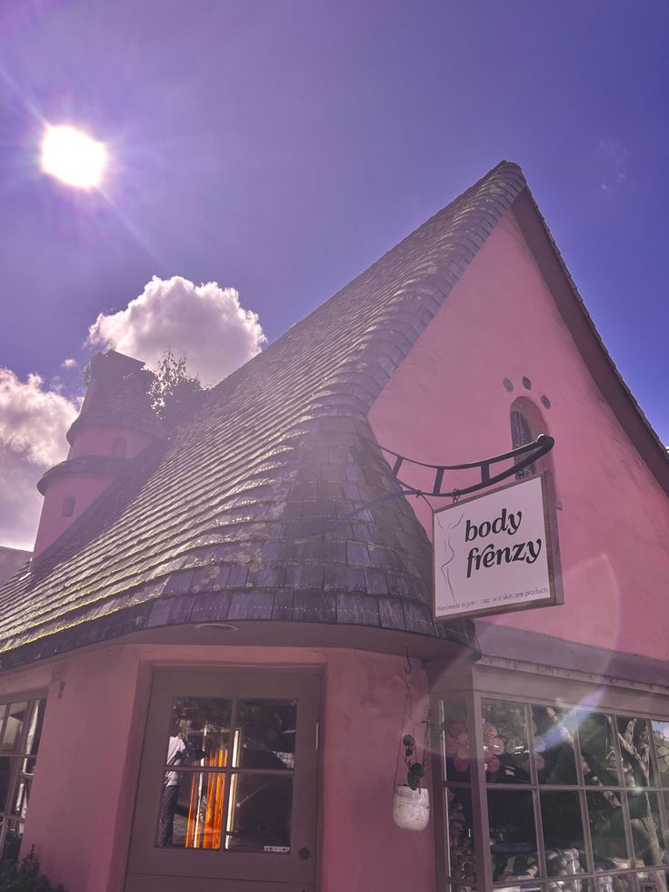 Pink cottage-style building with steep slate roof and shop sign under bright blue sunny sky