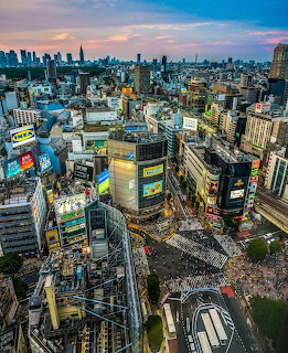 Aerial view of Shibuya Crossing in Tokyo with crowded streets, skyscrapers, and billboards at dusk.