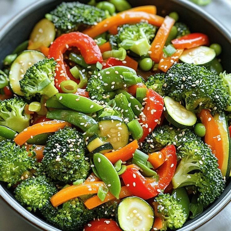 Bowl of mixed vegetables with broccoli, peppers, zucchini, snap peas, and sesame seeds