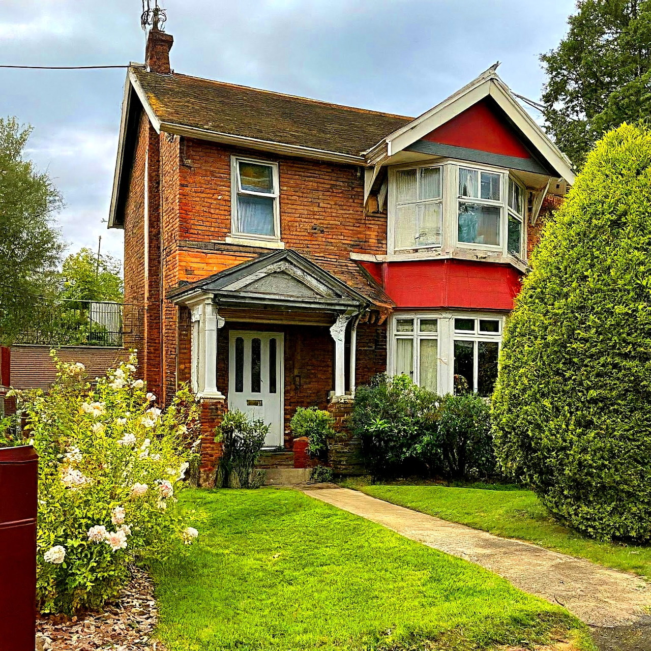 Victorian red brick house with white trim, bay window, and manicured front garden