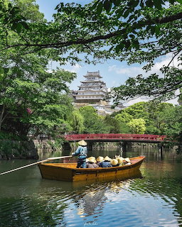 Wooden boat with passengers on the moat of Himeji Castle surrounded by green trees and a red bridge
