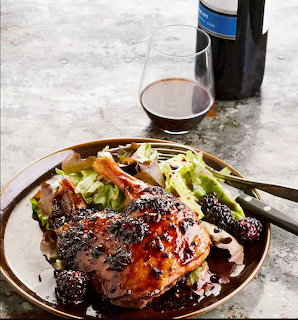 Plate of glazed roasted duck with green beans, blackberries, wine glass and bottle in background