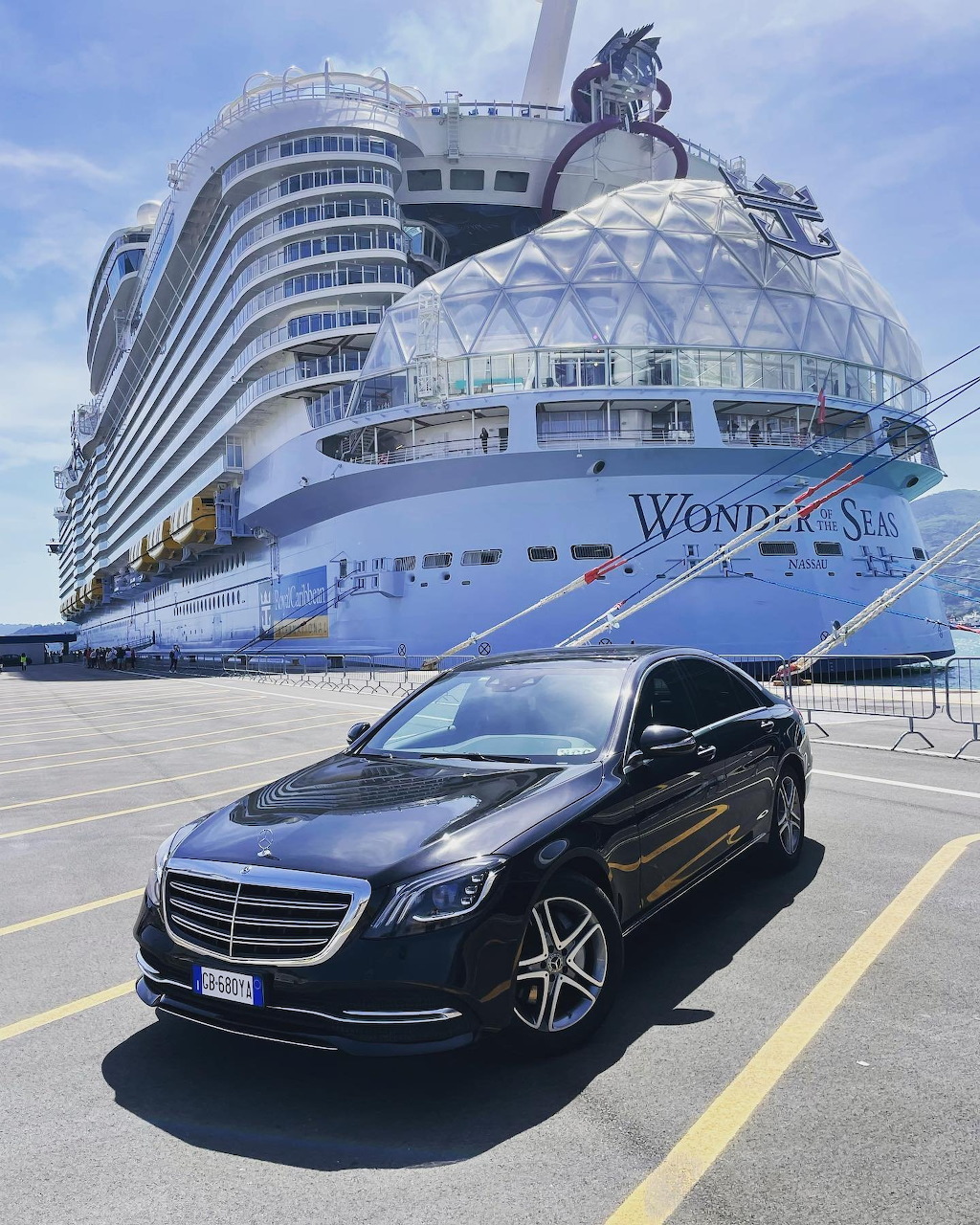 Black Mercedes sedan parked in front of a large white cruise ship at a sunny port