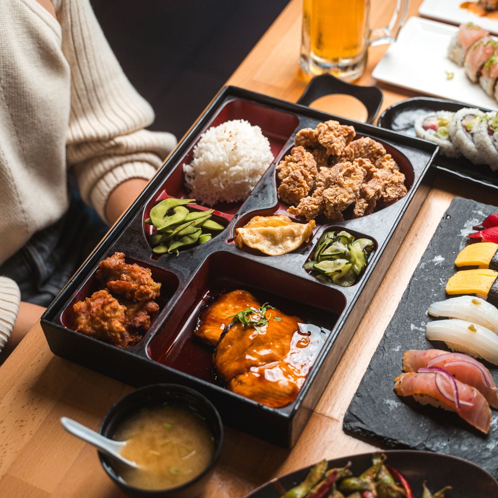 Japanese bento box with rice, fried chicken, pickles, sushi, and miso soup on a table