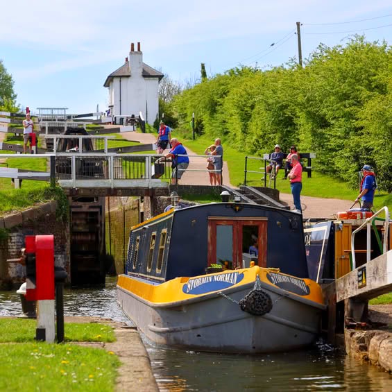 Yellow and blue narrowboat in canal lock with operators and green countryside