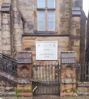 Historic stone building entrance with iron gate, steps, and a sign below a tall window