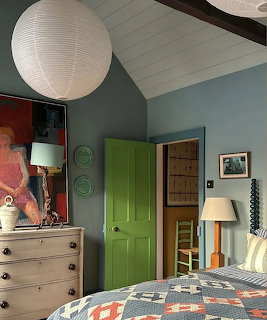 Cozy attic bedroom with green door, wooden dresser, paper lantern, and patterned quilt on bed