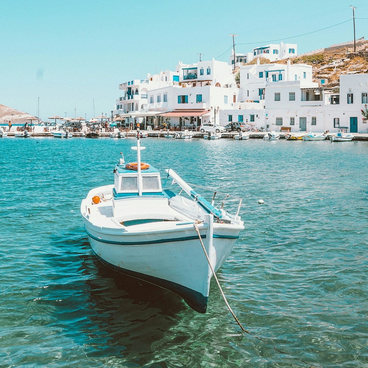 Small white boat in a sunny Greek harbor with white waterfront buildings