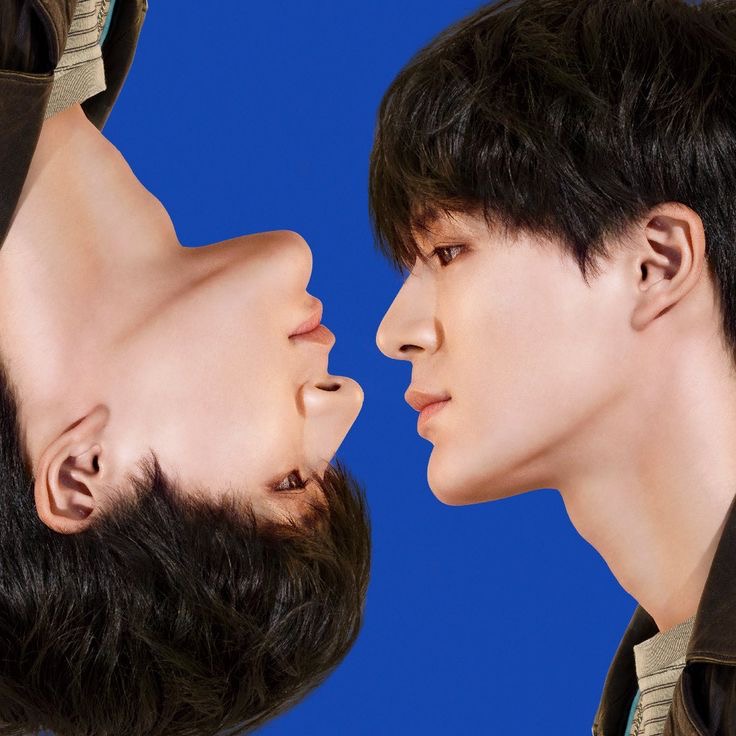 Two young people in profile, one upside down, facing each other against a blue studio background