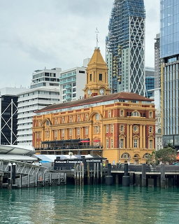 Historic Auckland Ferry Building with clock tower framed by modern glass skyscrapers at waterfront