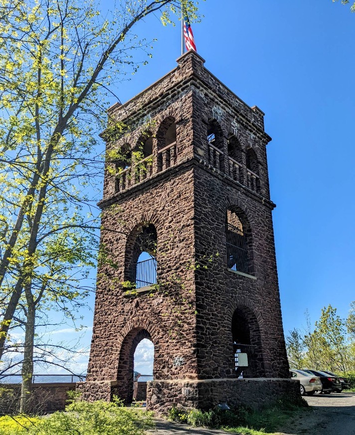 Tall stone tower with arched openings and American flag on top against blue sky