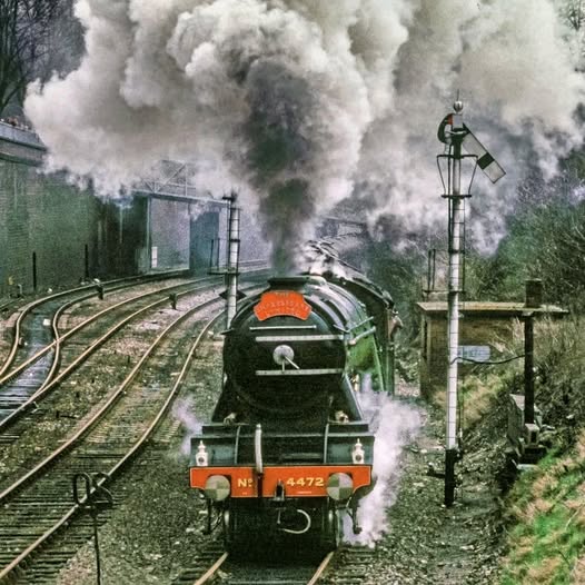 Black steam locomotive on tracks with large clouds of steam and smoke