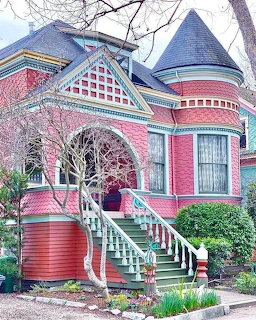 Colorful pink Victorian house with blue turet, ornate trim, and green staircase railings