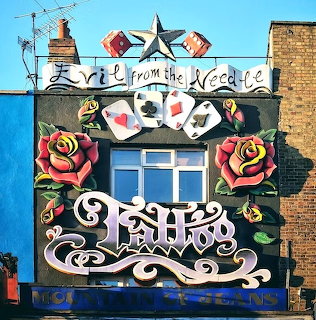 Elaborately decorated tattoo shop building facade with roses, skulls, playing cards, and ornamental text