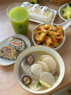 Korean meal with rice cake soup, kimchi, green tea, and assorted side dishes on a wooden table