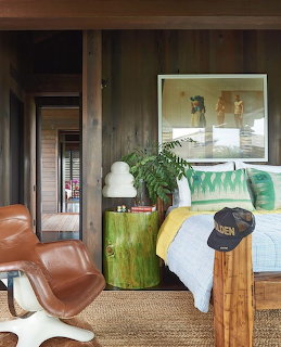 Rustic bedroom with dark wood walls, leather chair, green side table, and bed with colorful pillows