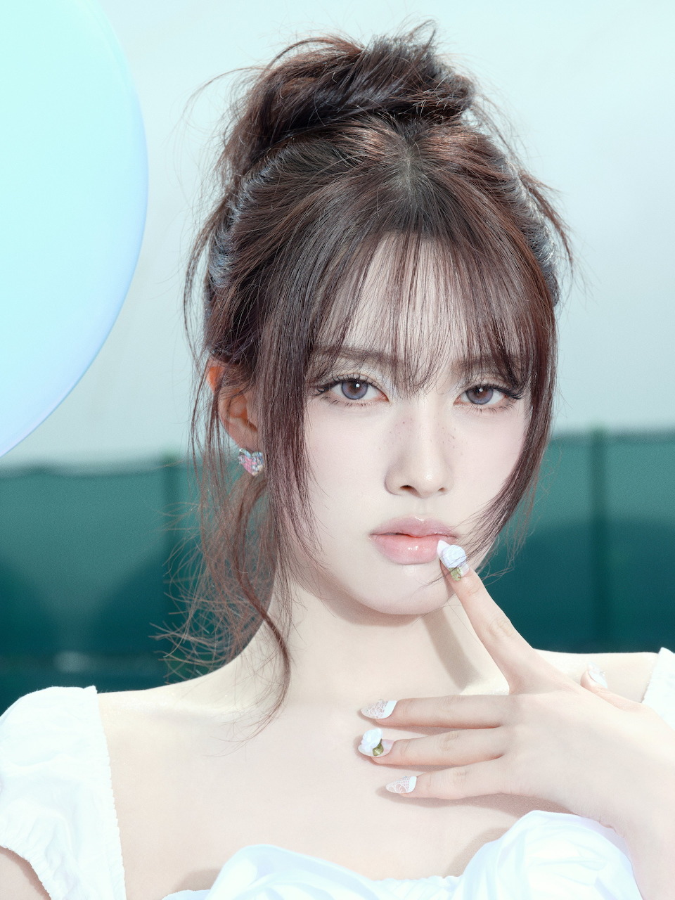 Portrait of young woman with brown hair updo, bangs, and bare shoulders against blue background