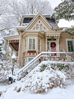 Snow-covered Victorian house with Christmas wreath on front door and white stairs leading to porch