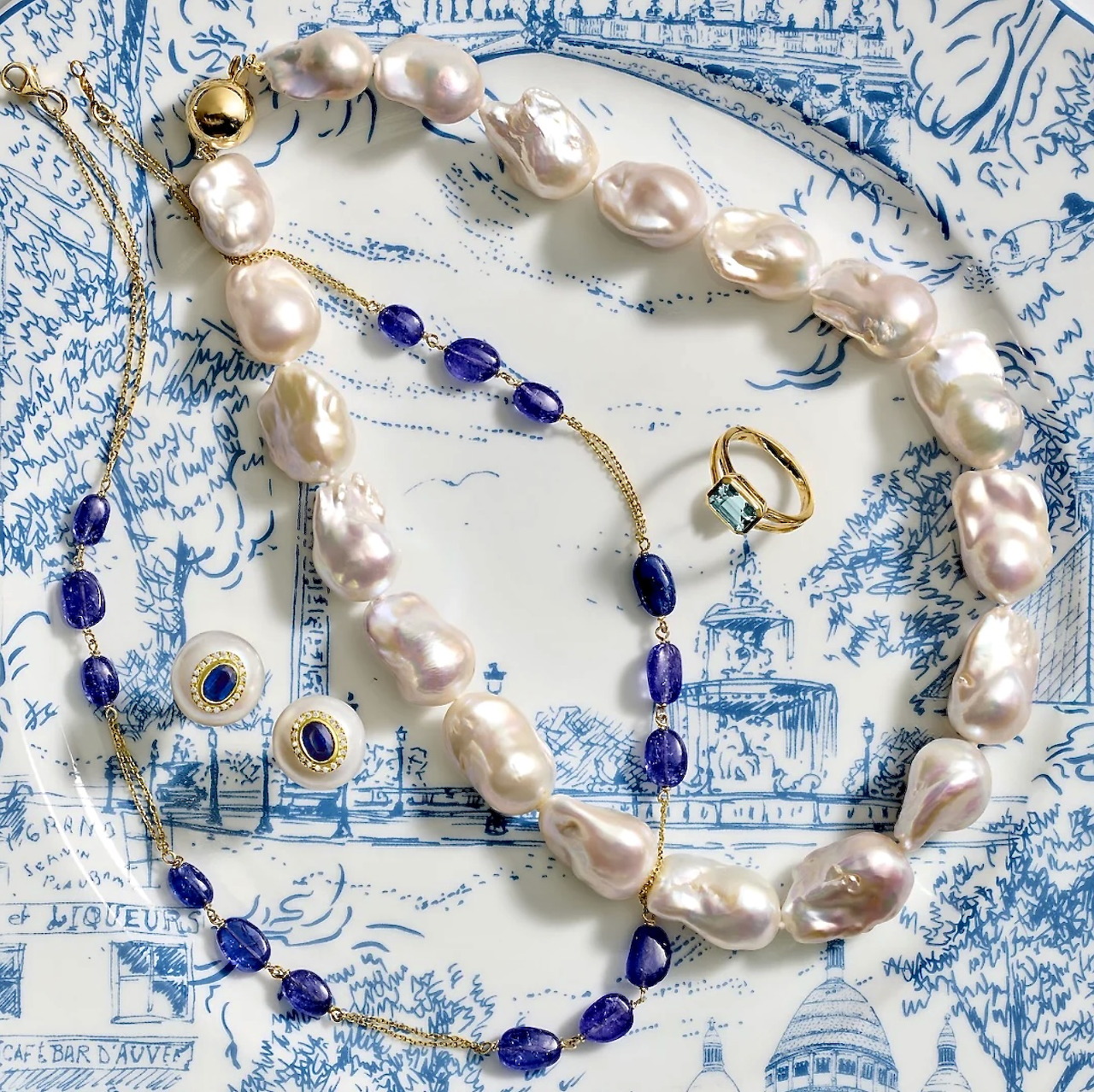 Pearl necklace with blue beads, rings, and evil eye charms on a blue and white patterned background