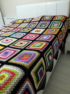 Bed with a colorful crocheted granny square bedspread in a simple bedroom