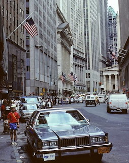 1980s New York City Wall Street scene with vintage cars, pedestrians, and neoclassical buildings with American flags