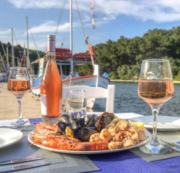 Seafood platter with prawns and wine glasses on waterfront table overlooking marina