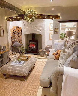 Cozy cottage living room with fireplace, plaid ottoman, cream furniture, and decorative garland