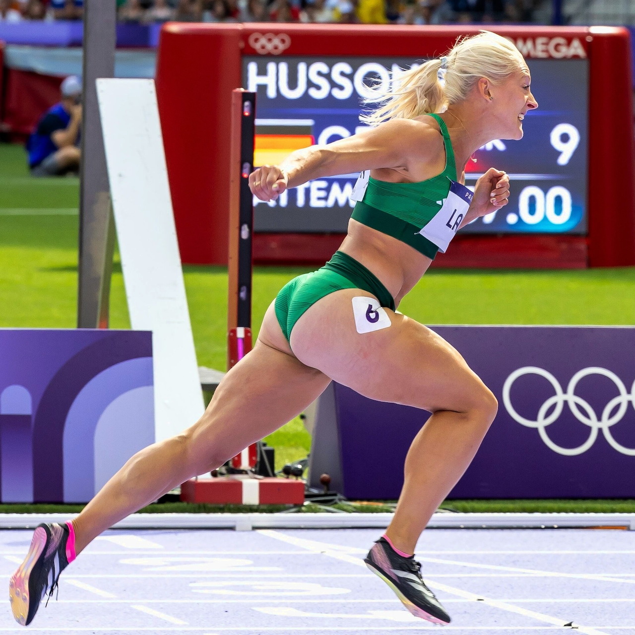 Female sprinter in green uniform exploding from starting blocks at Olympic track event