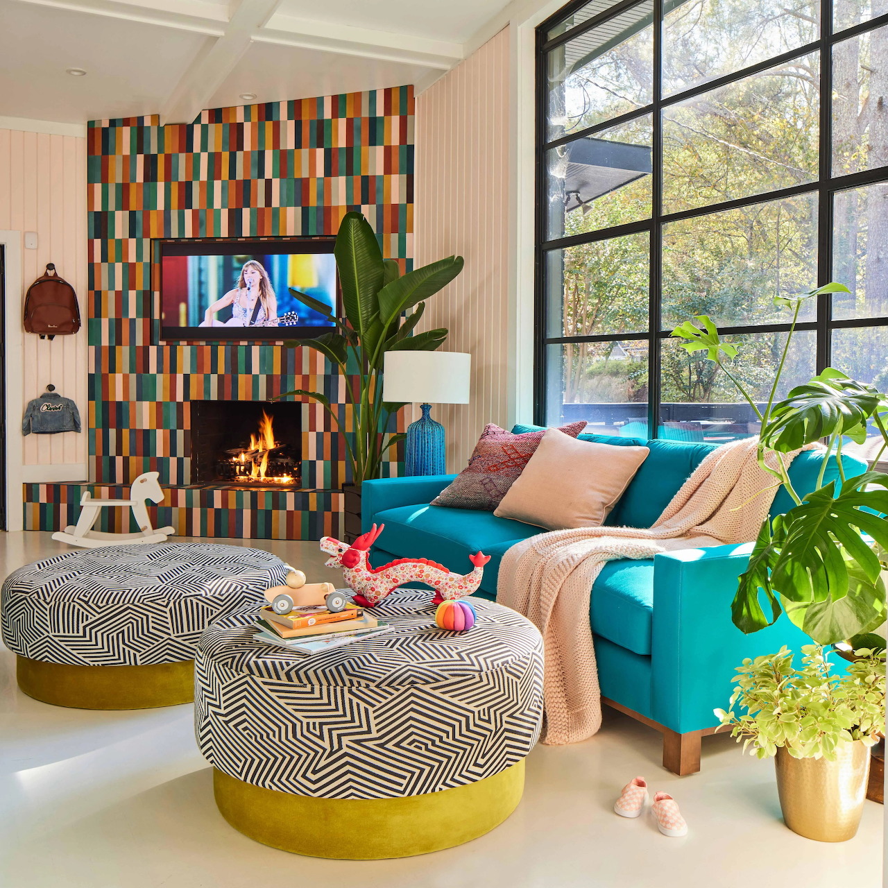 Modern living room with turquoise sofa, patterned ottomans, colorful mosaic wall, and plants