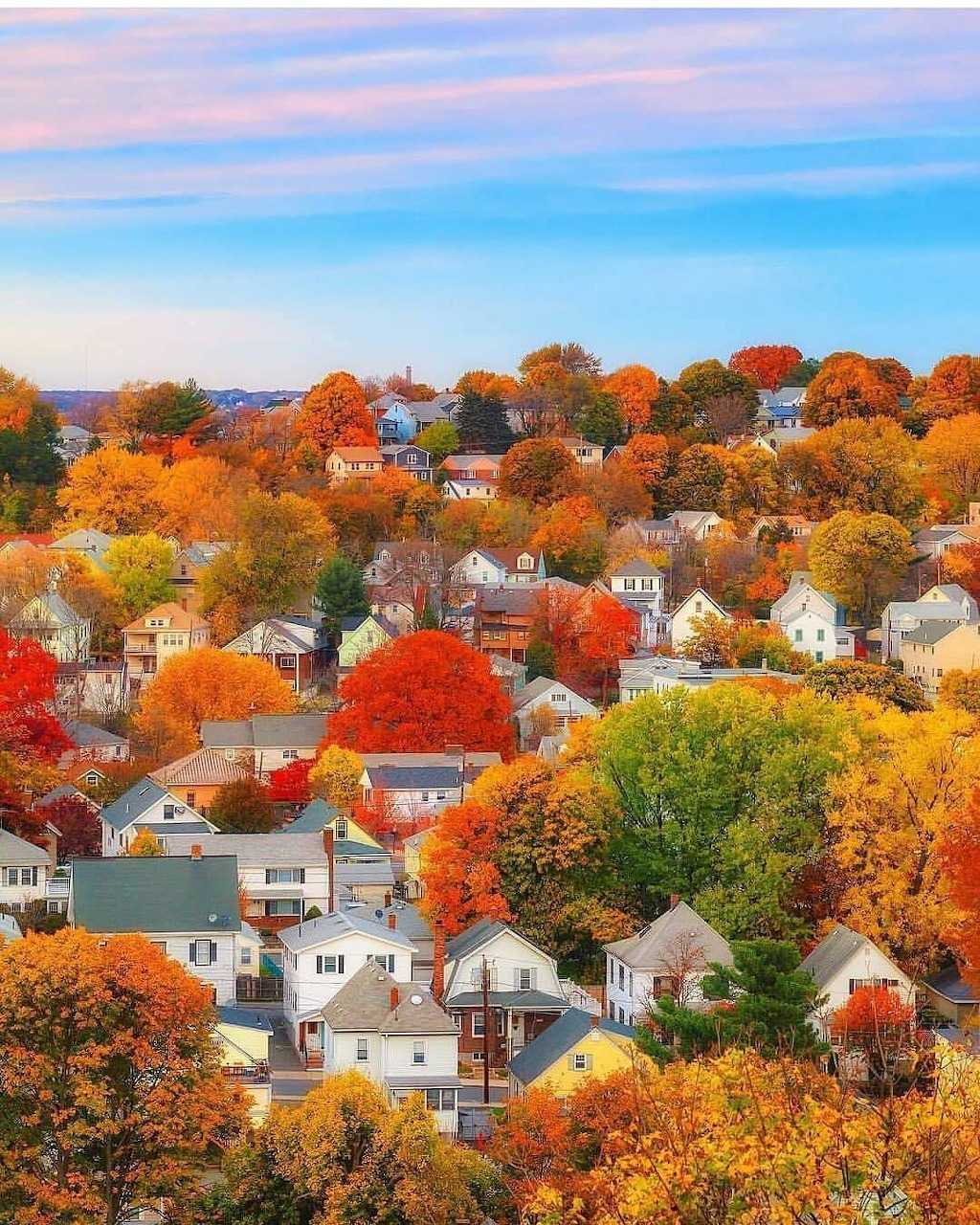 Aerial view of a town with houses nestled among colorful autumn trees under a pink and blue sky