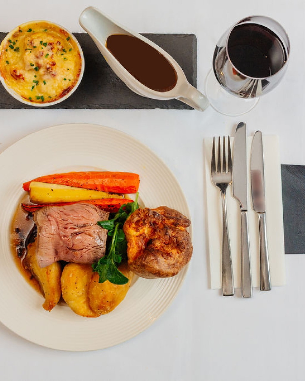 Plated roast dinner with meat, potatoes, vegetables, Yorkshire pudding, gravy, and red wine on a table