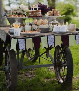 Rustic wooden cart with bunting holding tiered dessert stands and cupcakes outdoors