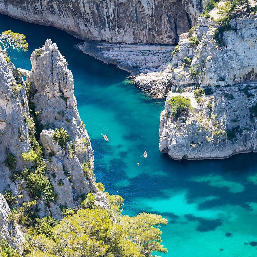 Aerial view of turquoise water between white limestone cliffs with boats in Cassis, France