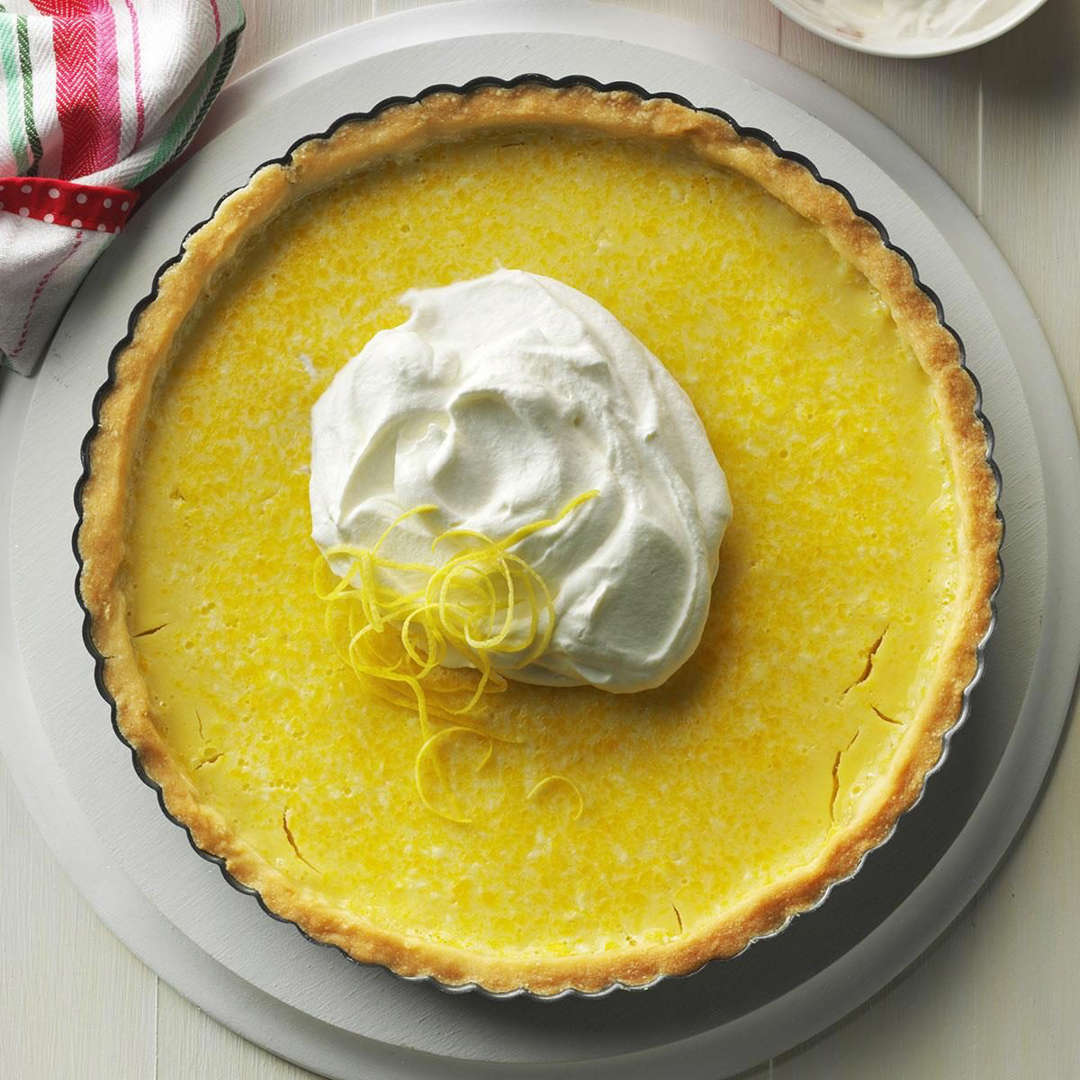 Overhead view of a lemon tart with whipped cream dollop and citrus zest on gray plate
