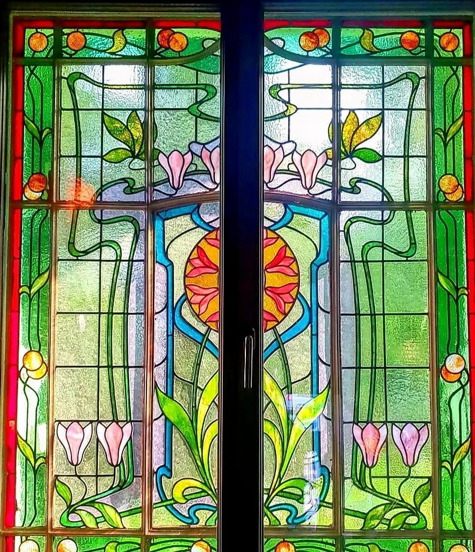 Art Nouveau stained glass window with flowers, green panels, and a colorful central design