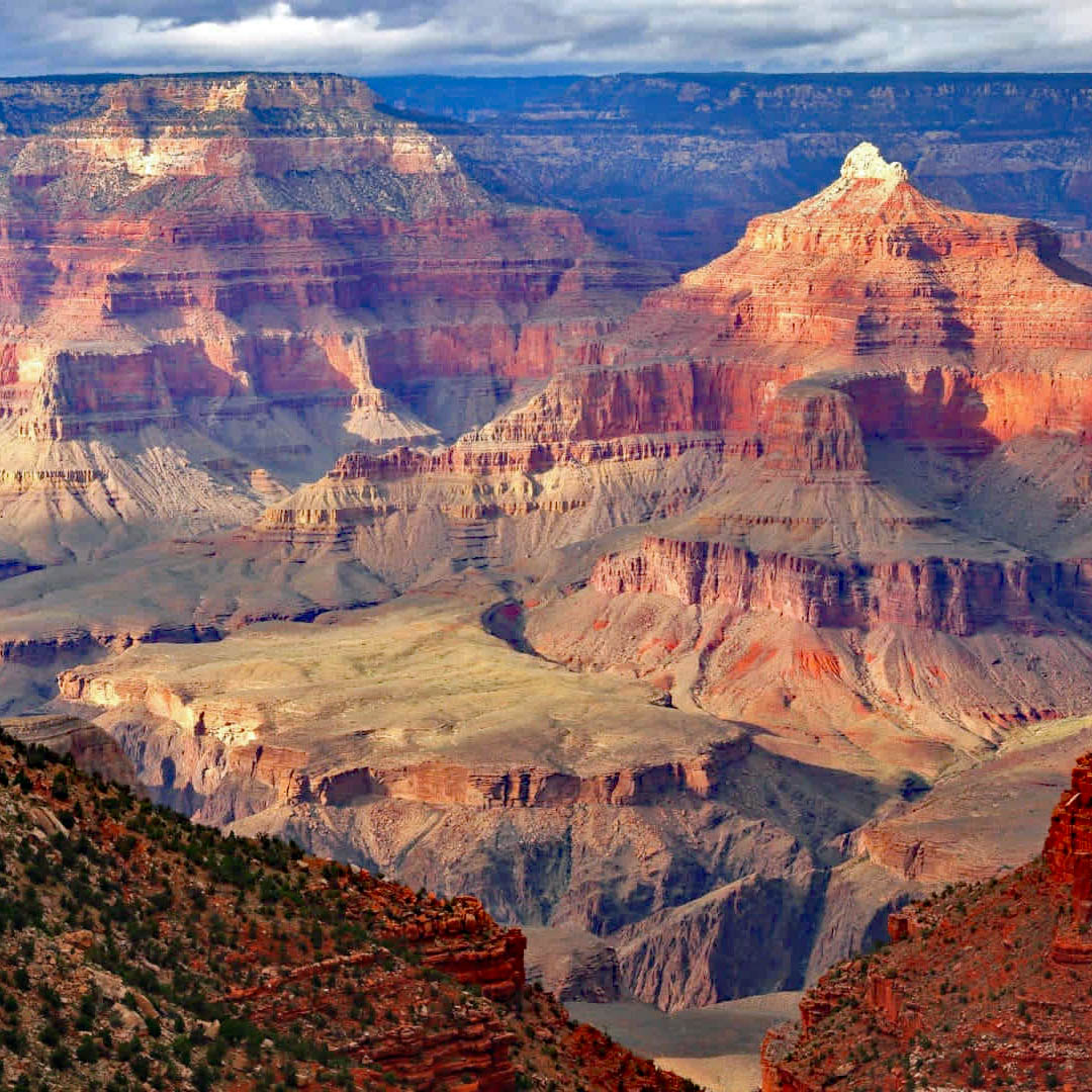 Layered red rock canyon cliffs and mesas under a cloudy blue sky