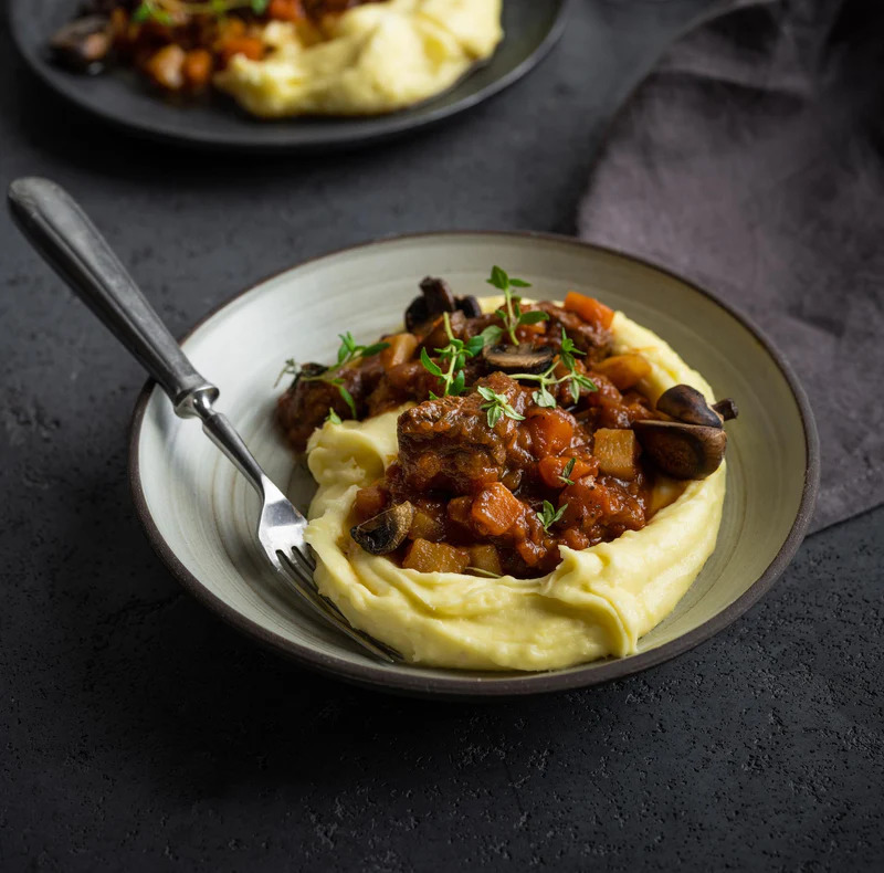Plate of ragout over mashed potatoes on a dark table with a fork