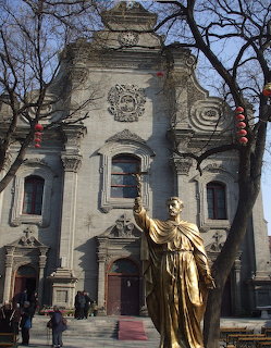 Historic cathedral facade in Beijing with a gold statue in front and leafless trees