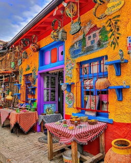 Brightly painted Greek taverna with orange walls, blue windows, checkered tablecloths, and colorful decorations