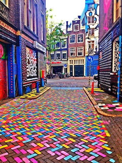 Colorful painted cobblestone street in Amsterdam with traditional Dutch buildings and graffiti art