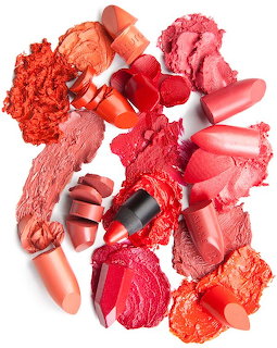Multiple red and pink lipsticks with crushed swatches spread on a white background