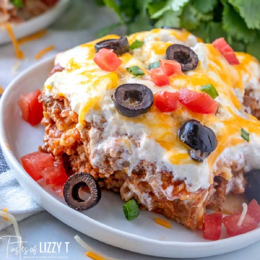 Mexican lasagna with cheese, olives, tomatoes, and green onions on white plate